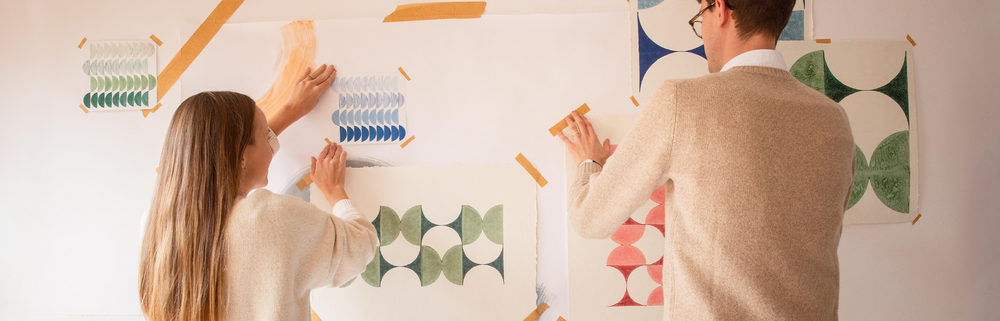 A woman and man sticking some art prints on a wall