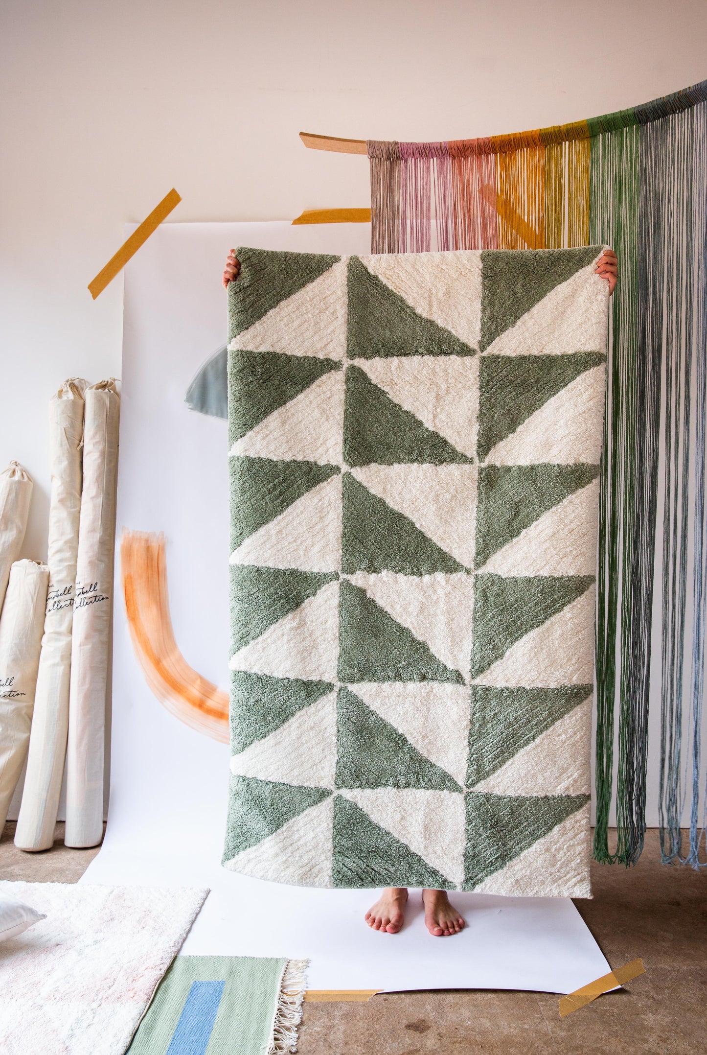 A person holding up a rug with a green and cream triangle pattern 