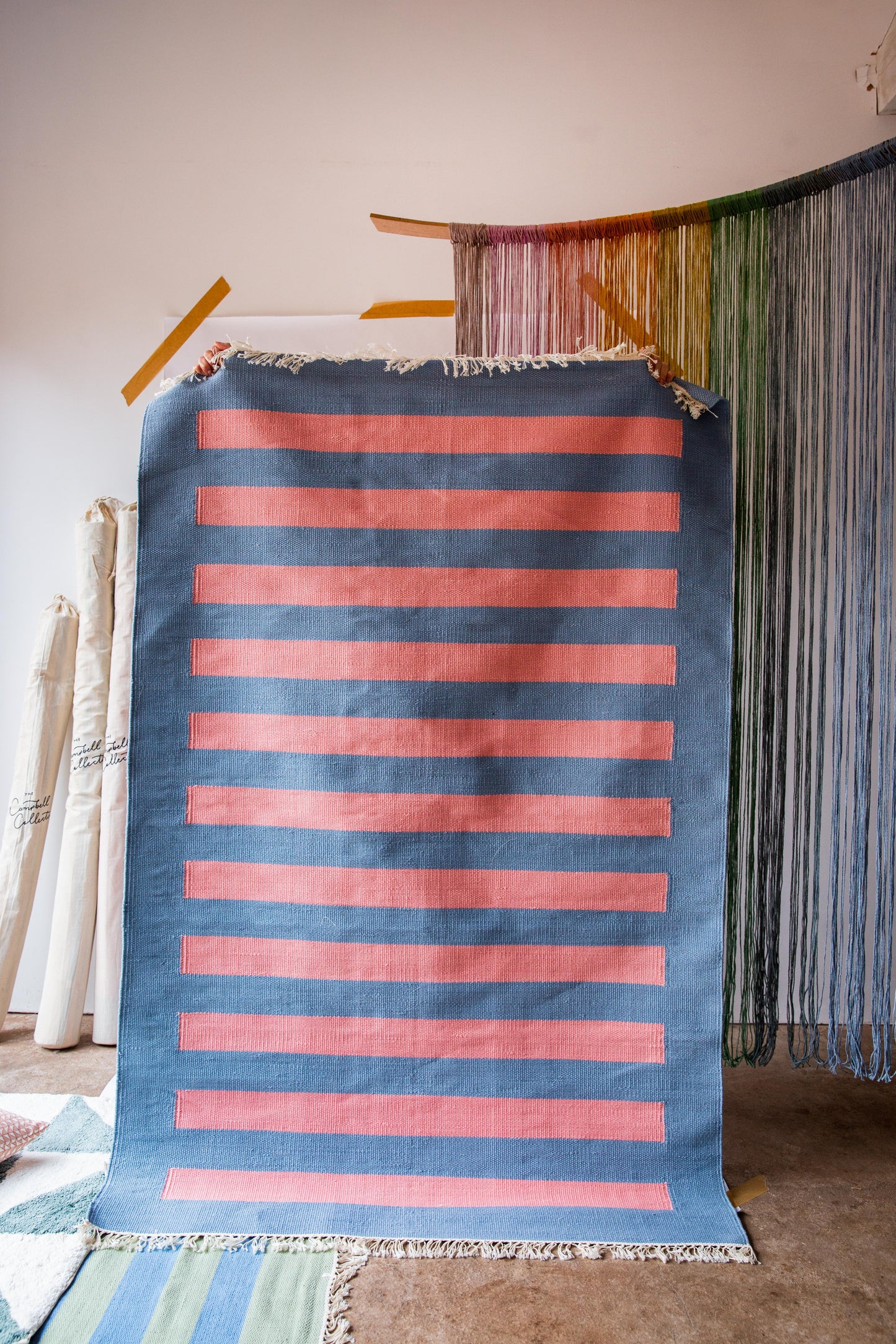 A person holding up a rug with a blue background and pink stripes on