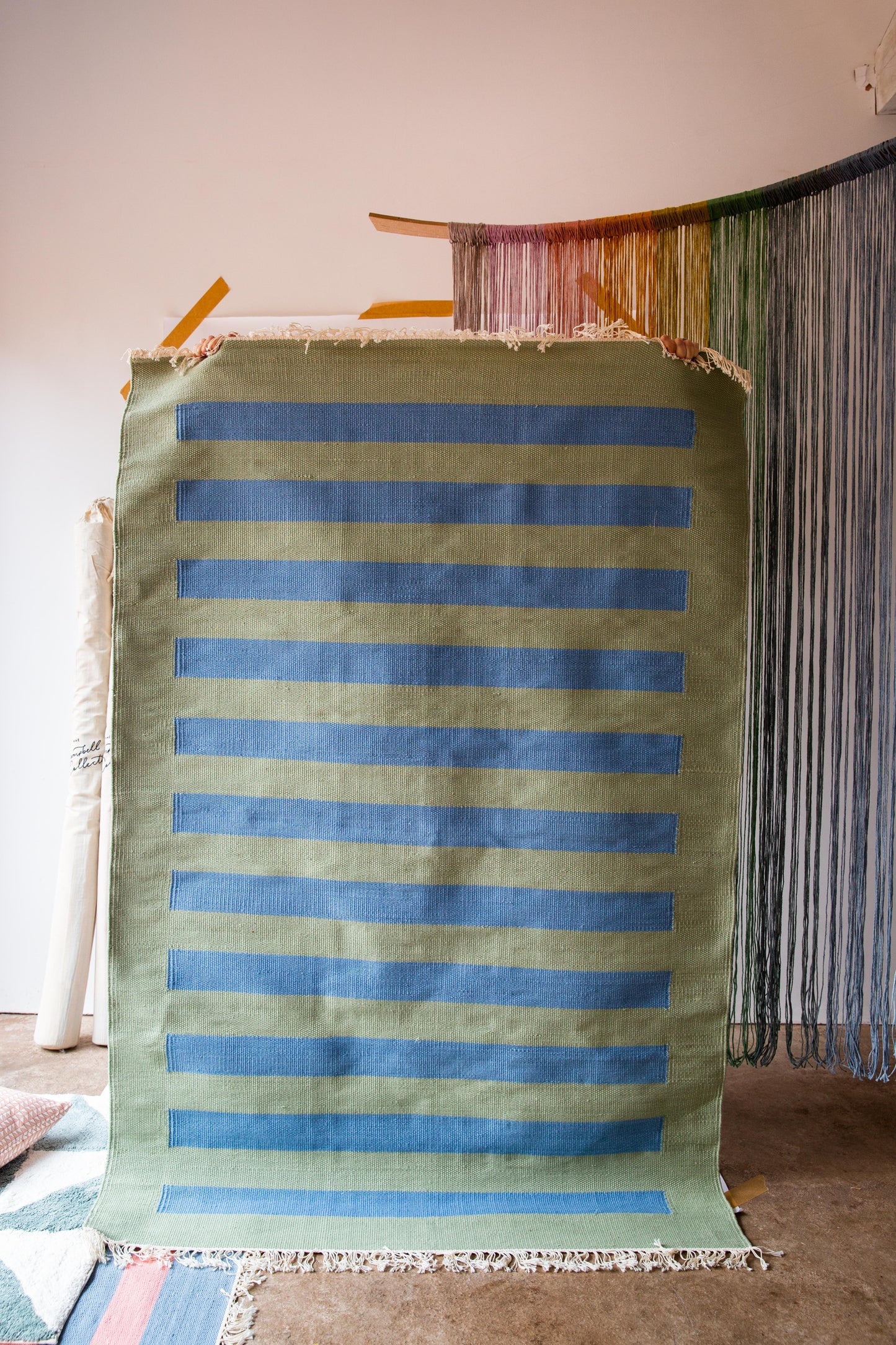 A person holding up a rug with a green background and blue stripes on