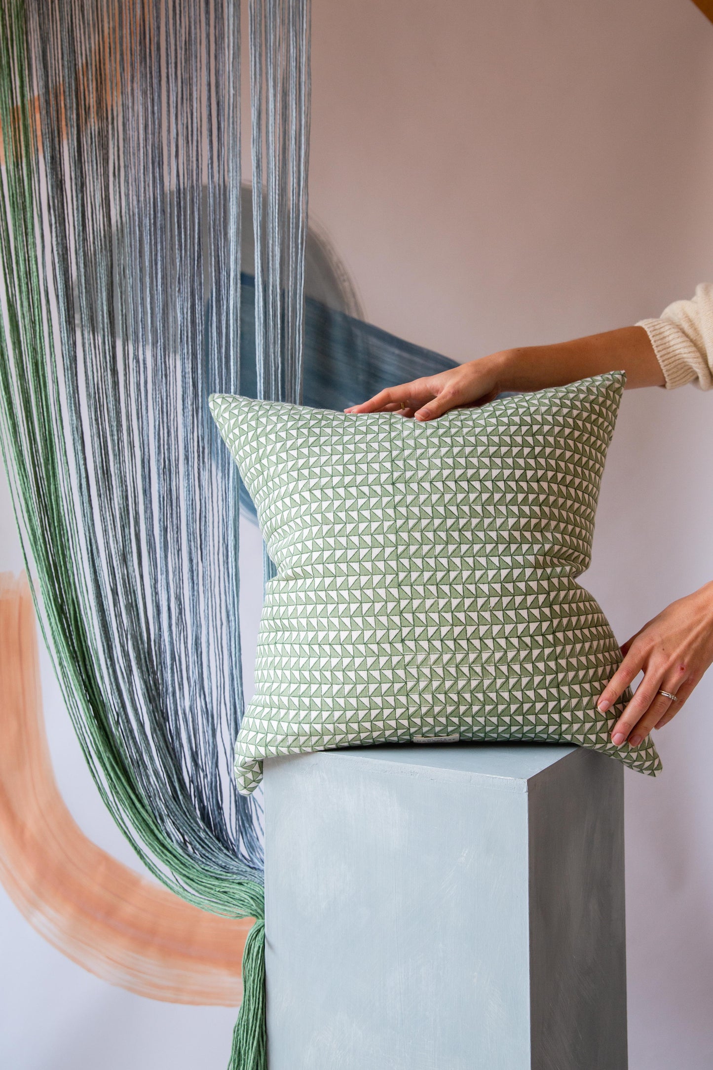 A square cushion with a green and cream triangle pattern on