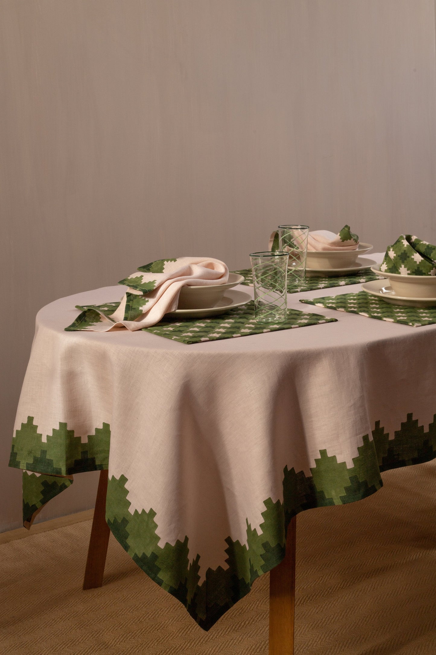 Pink tablecloth with green trim on a table under three place settings