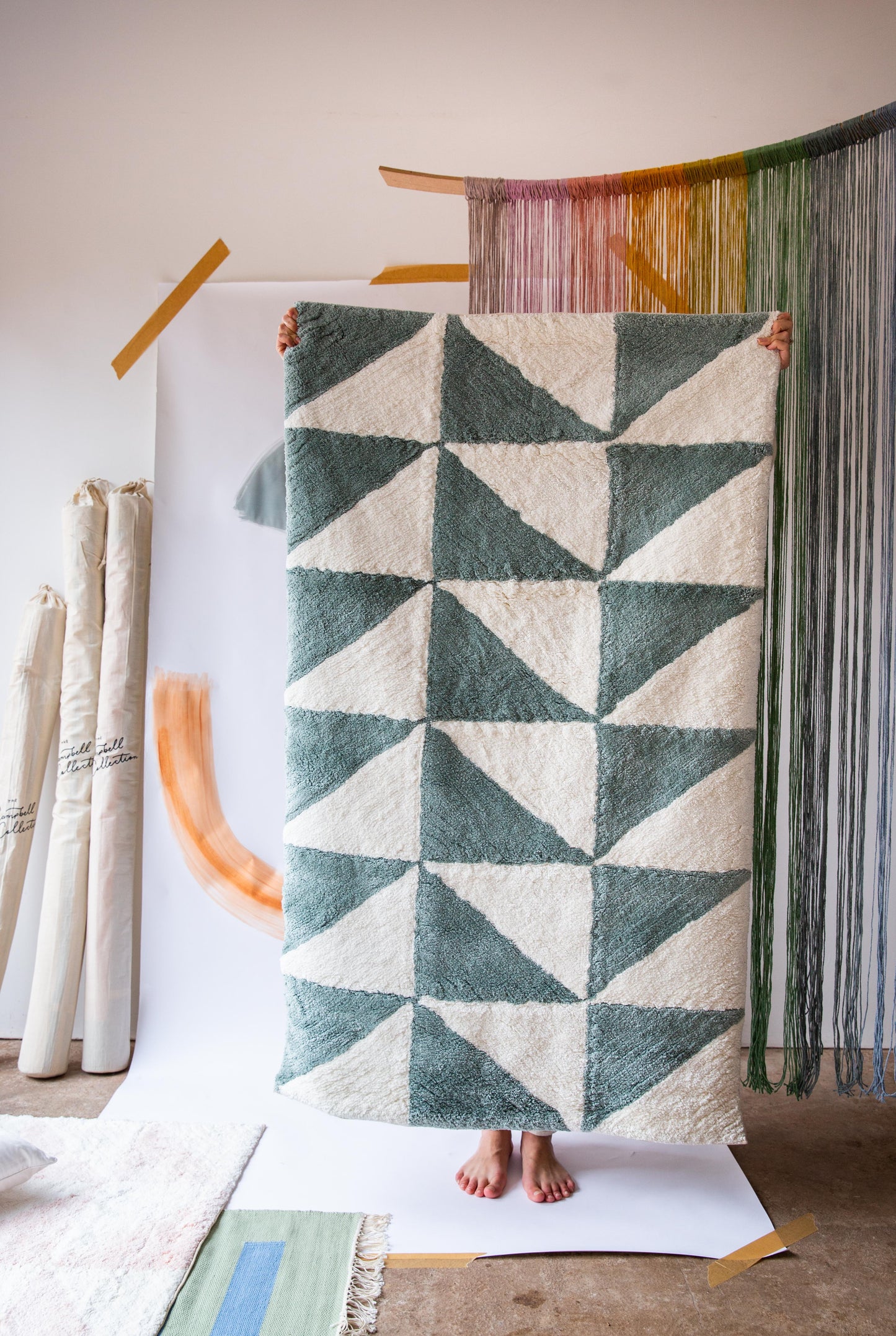 A person holding up a rug with a dark green and cream triangle pattern on